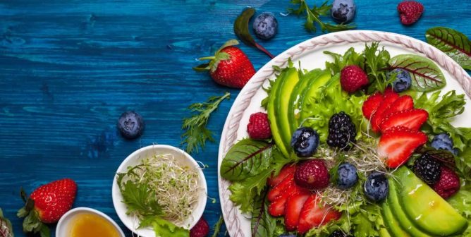 Salad with berries and avocados laid out on blue tabletop