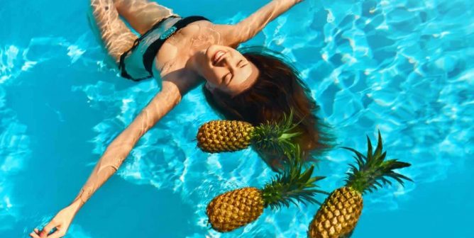 Woman floating in pool with several pineapples