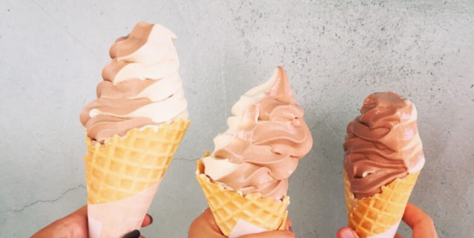 Three teenagers or women holding up vegan soft-serve ice cream cones.