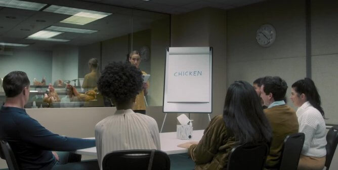 A focus group assembled around a note pad with the word "Chicken", with chickens observing from a recording booth in the background
