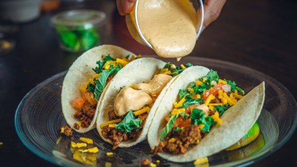 vegan taco trio on a plate with sauce being poured on