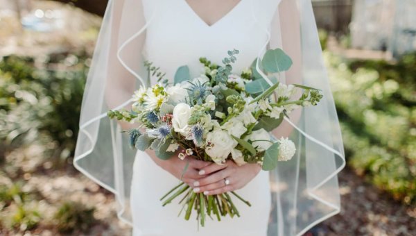 A bride in a white dress and veil holds a bouquet of flowers