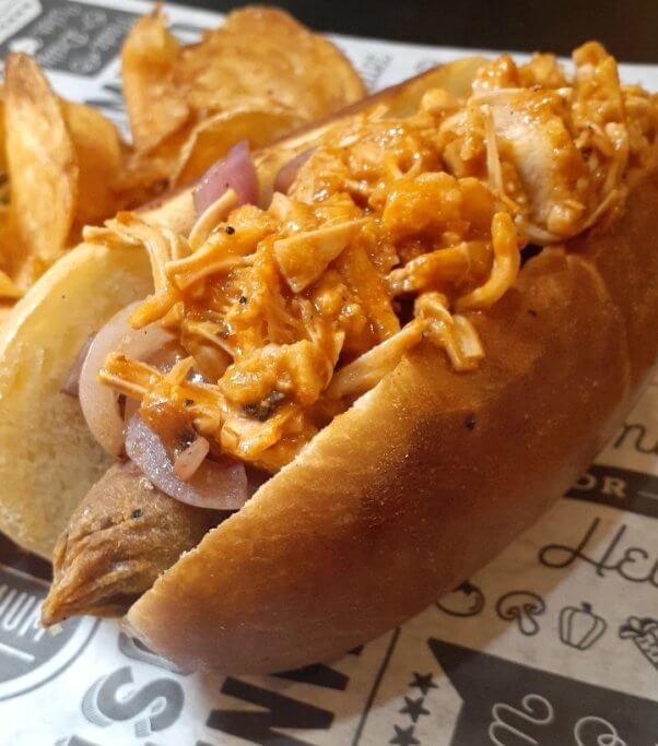 vegan sausage in a bun topped with buffalo jackfruit and onions