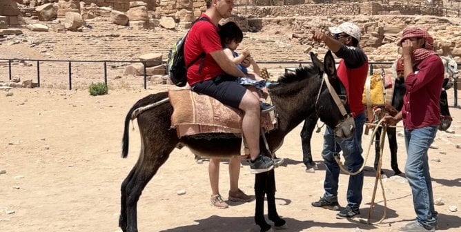 A tourist and a child sitting on a donkey's back