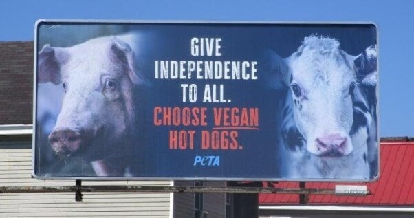 Photo of billboard with images of a pig and a calf. Text reads give independence to all. Choose vegan hot dogs.