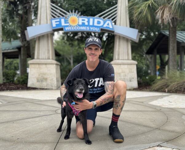 Man posing with a black dog in front of a 'Welcome to Florida' sign