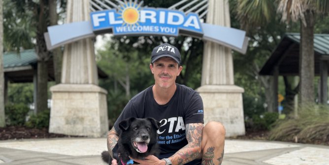 Man posing with a black dog in front of a 'Welcome to Florida' sign