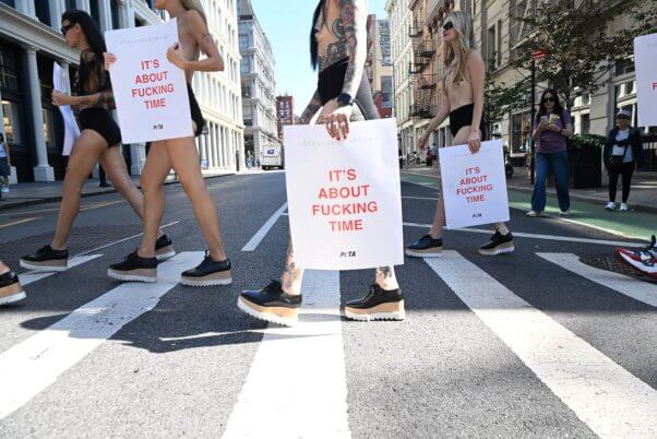 people walking on the street holding signs saying "it's about fucking time" in stella mccartney demo