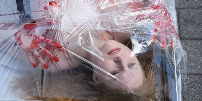 Close up of woman under plastic sheet with bloody hands