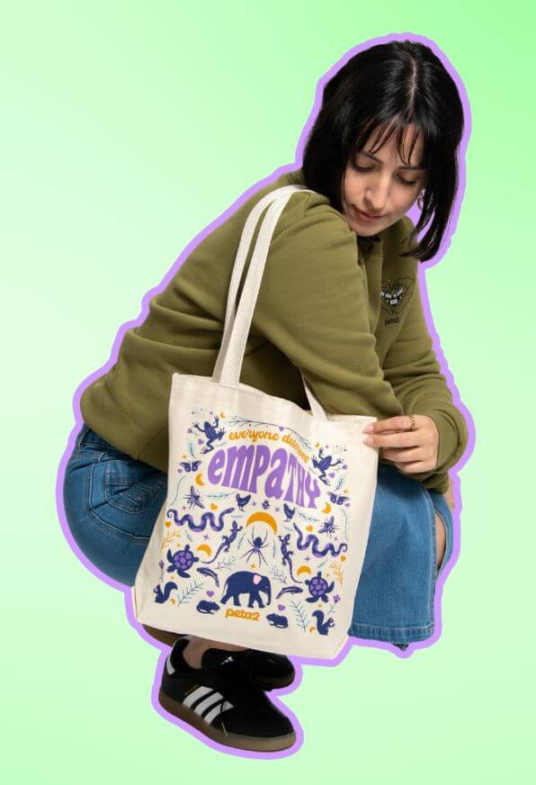 A person crouching down and wearing a peta2 empathy tote